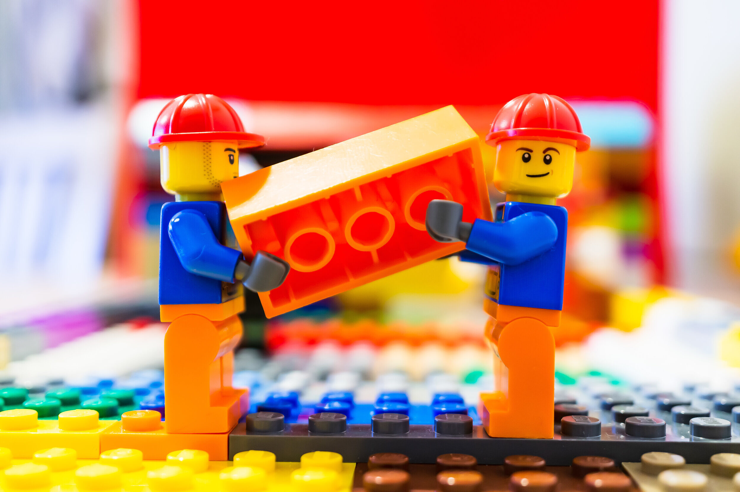 two-lego-construction-workers-carrying-together-a-orange-brick-on-march-14-2019-in-poznan-poland