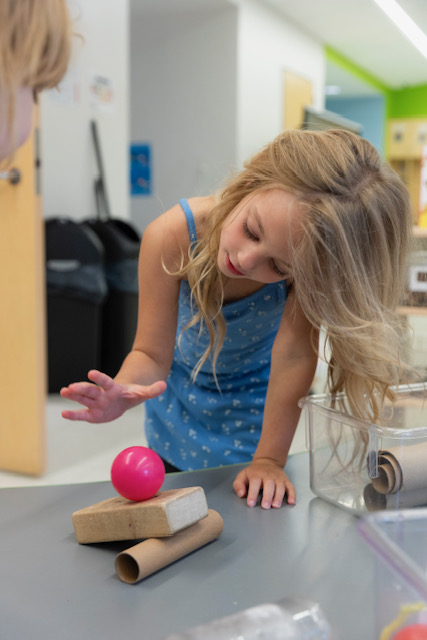 Young girl testing physics of pink ball on wooden block at New E3 School