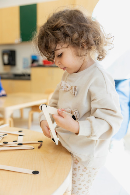 In a classroom, a young child joyfully builds with wooden blocks, showcasing her creativity and focus.
